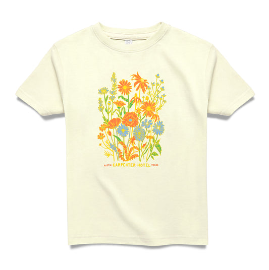 A beige kids' t-shirt with a colorful floral graphic design and text that says ' CARPENTER HOTEL AUSTIN TEXAS' on the chest