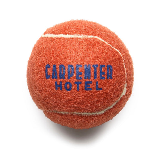 An orange tennis style dog ball with 'CARPENTER HOTEL' printed in blue text on it.