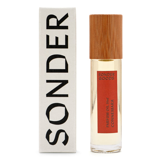 A small, clear glass bottle with a wooden cap, labeled 'Sonder Goods Parfum Oil Connemara', next to its white box packaging with the word 'SONDER' in black text.